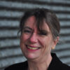 Photo of Helen Rimington, PhD - smiling brunette with her hair pulled back. Grey textured background wall.